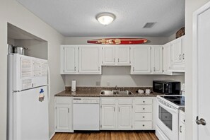 Cocina compacta con gabinetes blancos, encimera de granito, horno microondas integrado y lavavajillas.