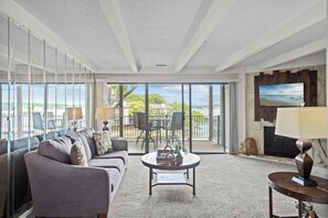 Una sala de estar con sofá, mesa de centro y chimenea. Cuenta con un balcón con vista al océano.