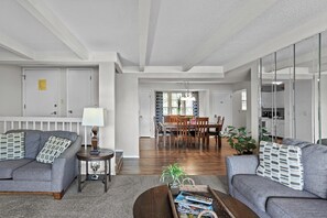 A modern living room with grey sofas, a coffee table, and a dining area with wooden chairs and a table.