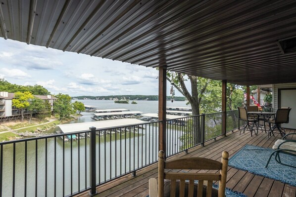 A covered deck with a view of a lake, docked boats, and a distant shoreline.