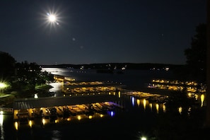 A nighttime view of a marina with boats docked, a bridge, and buildings with lights reflecting on the water.