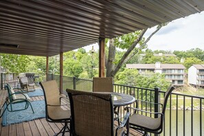 A covered outdoor deck with wicker furniture, a grill, and a view of a residential area. - Water's Edge 29-2A - Two Bedroom Apartment, Sleeps 6 (Lake Ozark)
