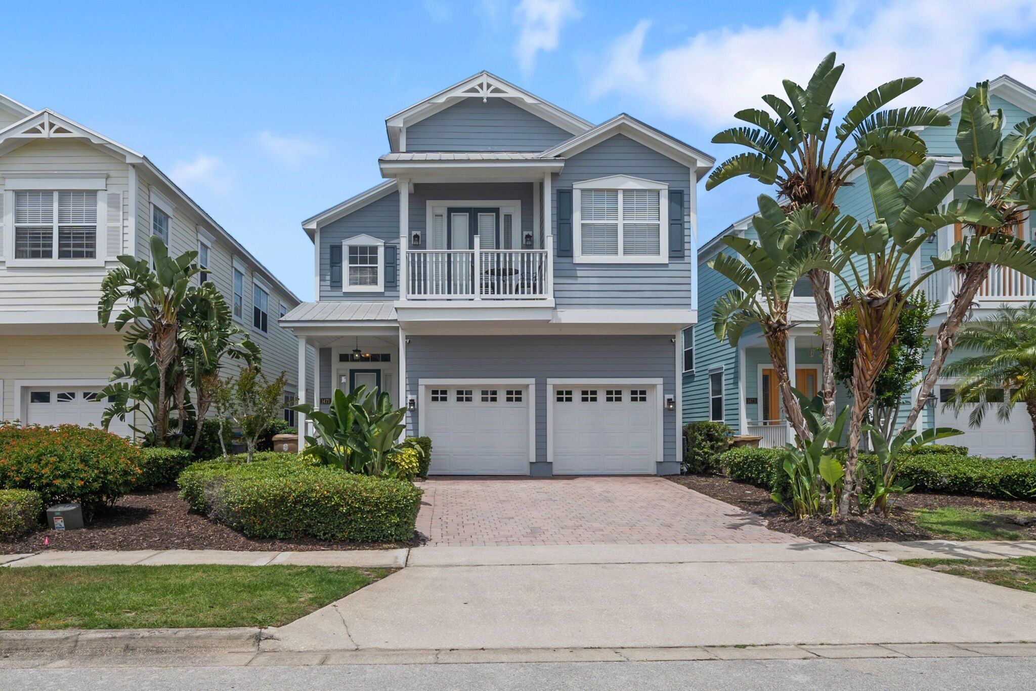 A two-story residential building with a balcony, a garage, and a well-maintained garden with various plants.