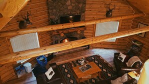 Interior de una cabaña de madera con chimenea de piedra, vigas de madera y una zona de estar acogedora.
