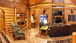Interior de una cabaña de troncos con chimenea, muebles de madera y pared de piedra.