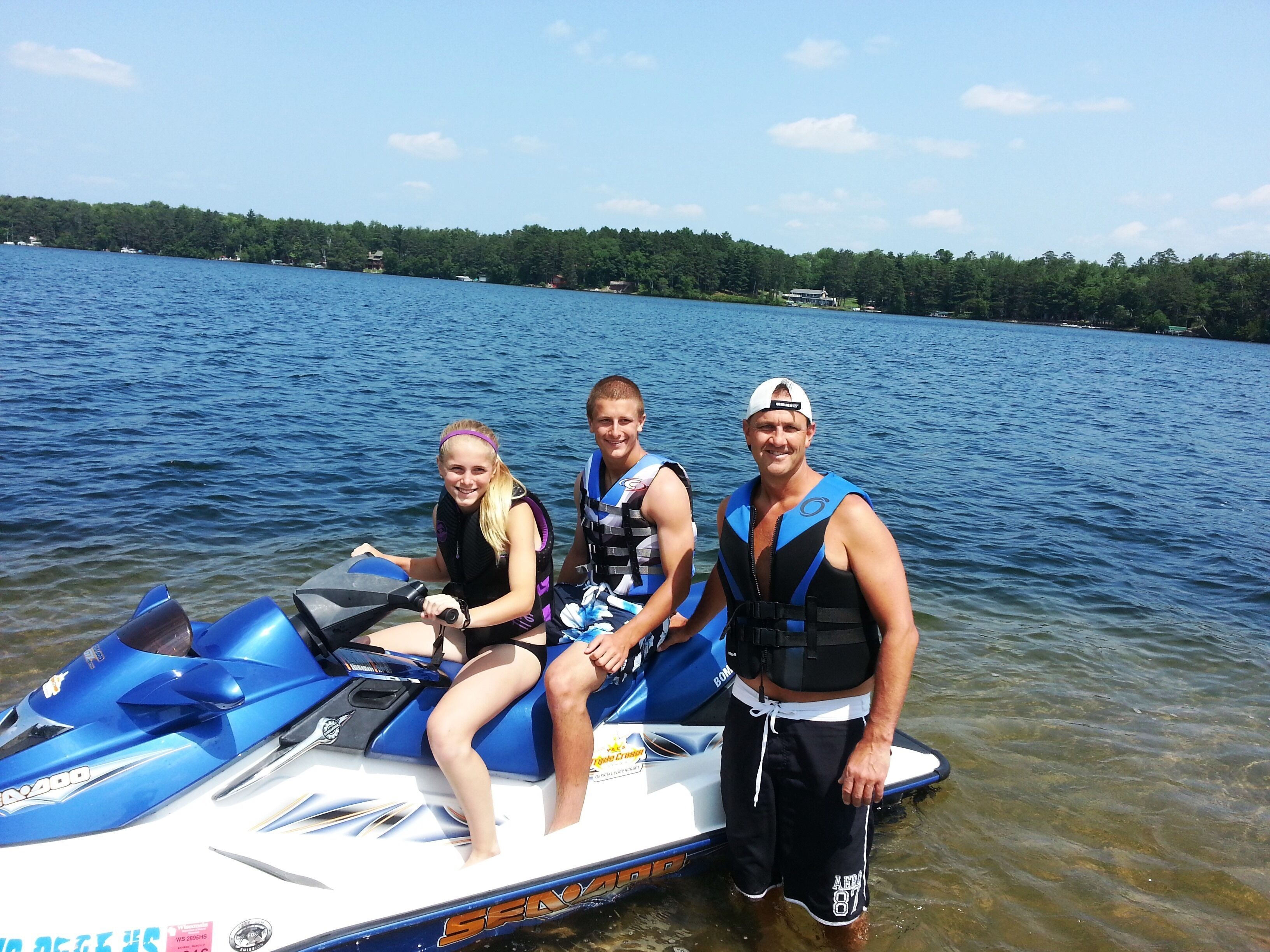 Three people on a jet ski with a lake and forest in the background.