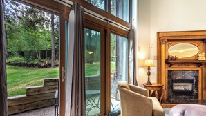 Un salón acogedor con chimenea, un sillón cómodo y vistas a un jardín exuberante a través de grandes puertas correderas de vidrio.