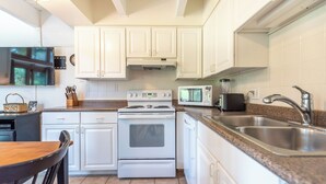 Una cocina con gabinetes blancos, estufa, microondas y fregadero.