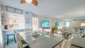 A modern living room with a dining area, a television, and a ceiling fan. - Island Escape 201 Affordable Condo (Clearwater Beach)