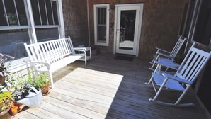 A wooden deck with white rocking chairs and a bench, surrounded by potted plants.