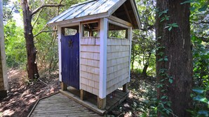 A wooden structure with a sloped roof, situated in a wooded area.