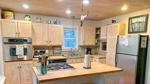 A modern kitchen with wooden cabinets, a stainless steel oven, a gas stove, and a refrigerator.