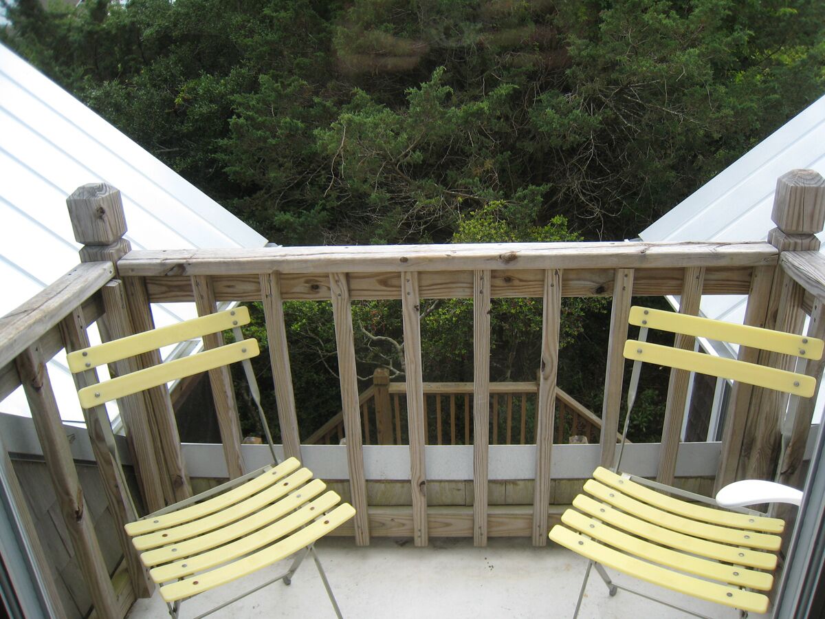 A wooden deck with two yellow chairs and a wooden table.