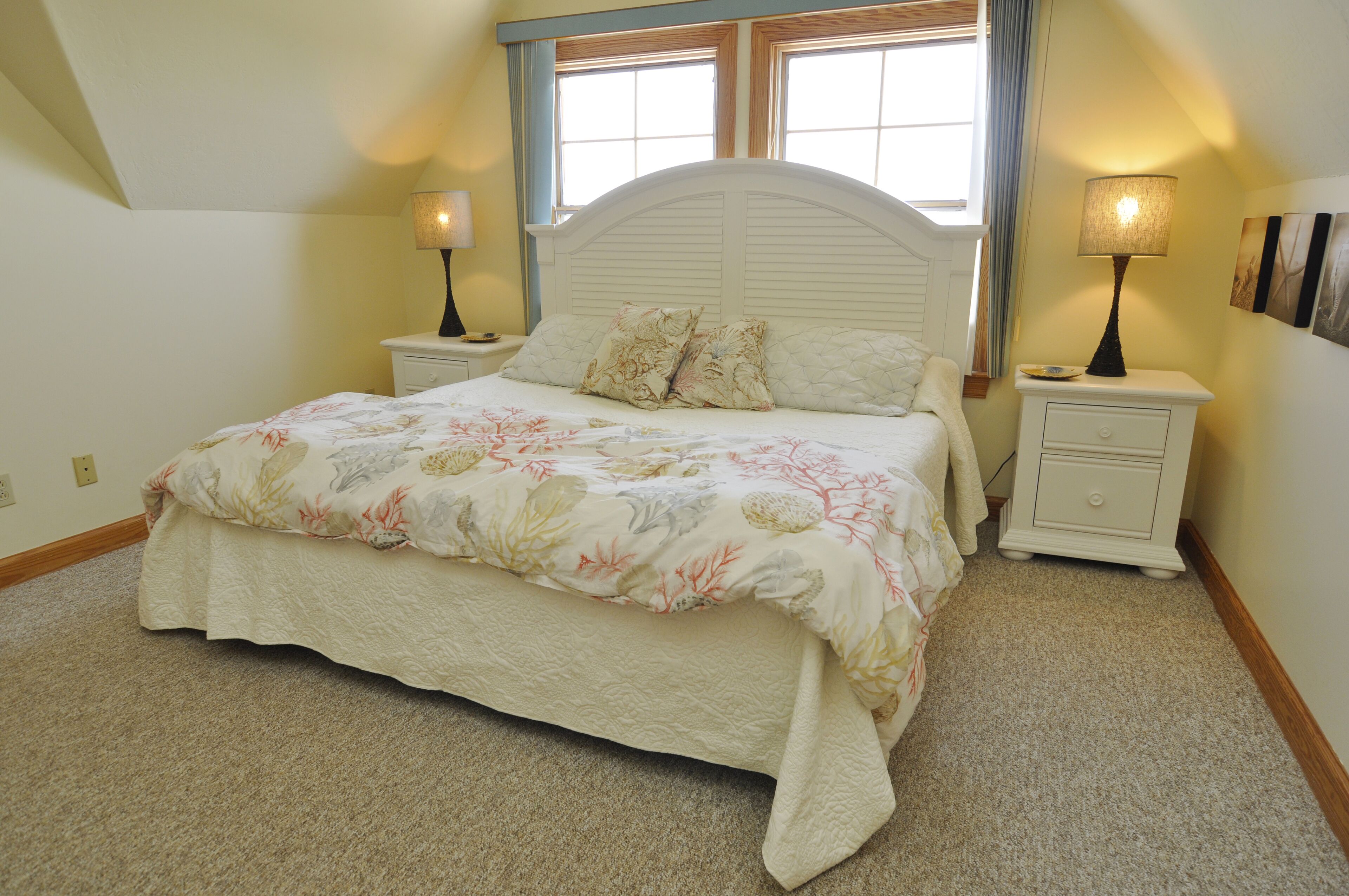 Une chambre à coucher comprenant un lit, deux tables de chevet, une commode, une fenêtre et une lampe fixée au mur.