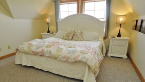 Une chambre à coucher comprenant un lit, deux tables de chevet, une commode, une fenêtre et une lampe fixée au mur.