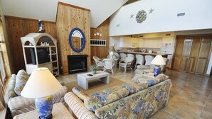Un salon avec des meubles en osier, une cheminée et une cuisine à l’arrière-plan.