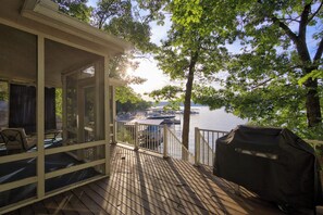 Una terraza techada con una parrilla, sillas y vista a barcos en un lago.
