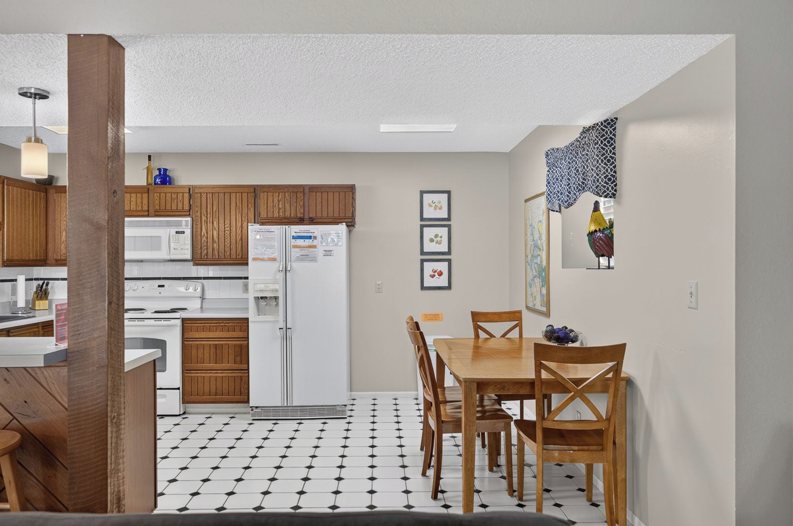 Una cocina con armarios de madera, un refrigerador blanco, una mesa de comedor con sillas y un piso con diseño.