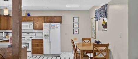 Una cocina con armarios de madera, un refrigerador blanco, una mesa de comedor con sillas y un piso con diseño.