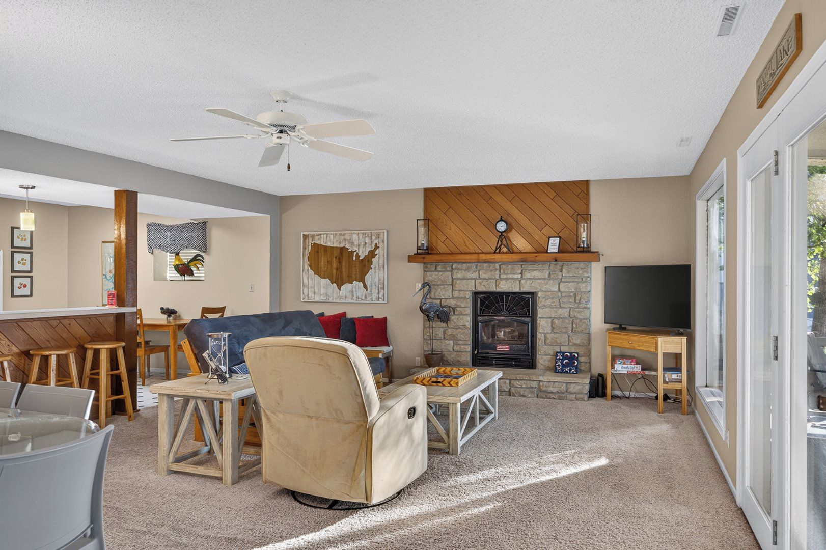 A living room with a stone fireplace, a ceiling fan, and a television.