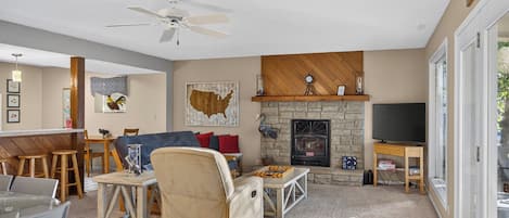 A living room with a stone fireplace, a ceiling fan, and a television.