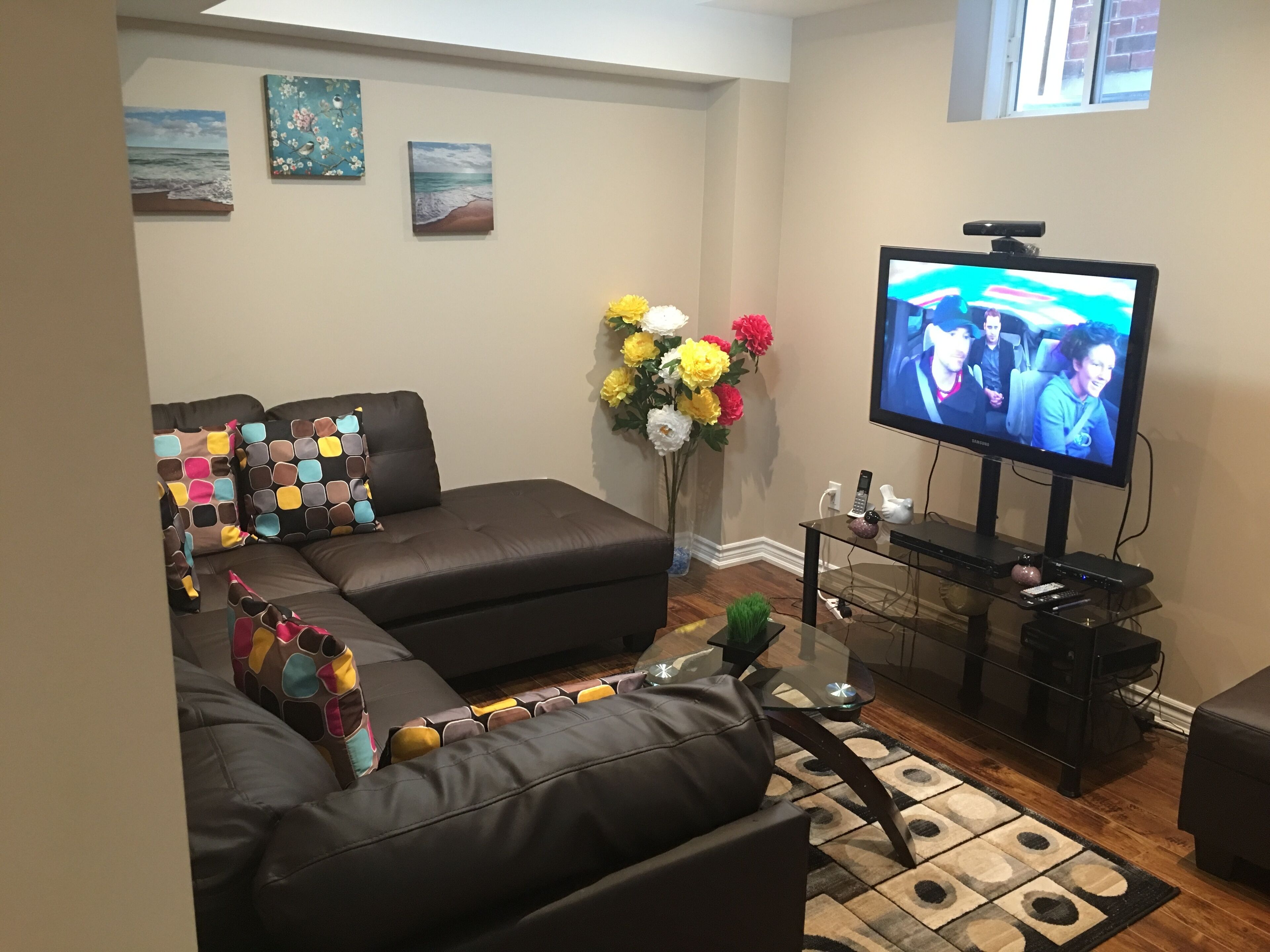 A living room with a brown leather sofa, a glass coffee table, and a flat-screen TV.