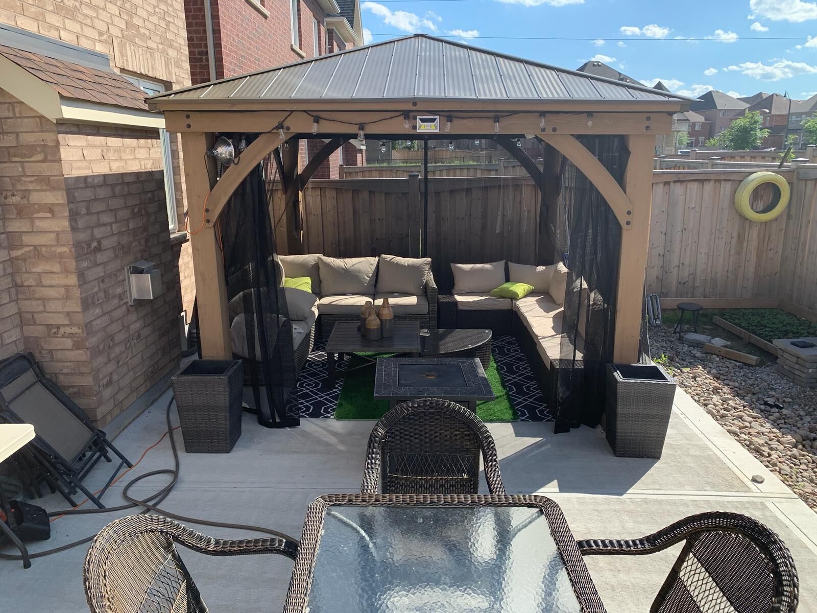 Een overdekt terras met een bank en stoelen, een glazen tafel en een pergola.