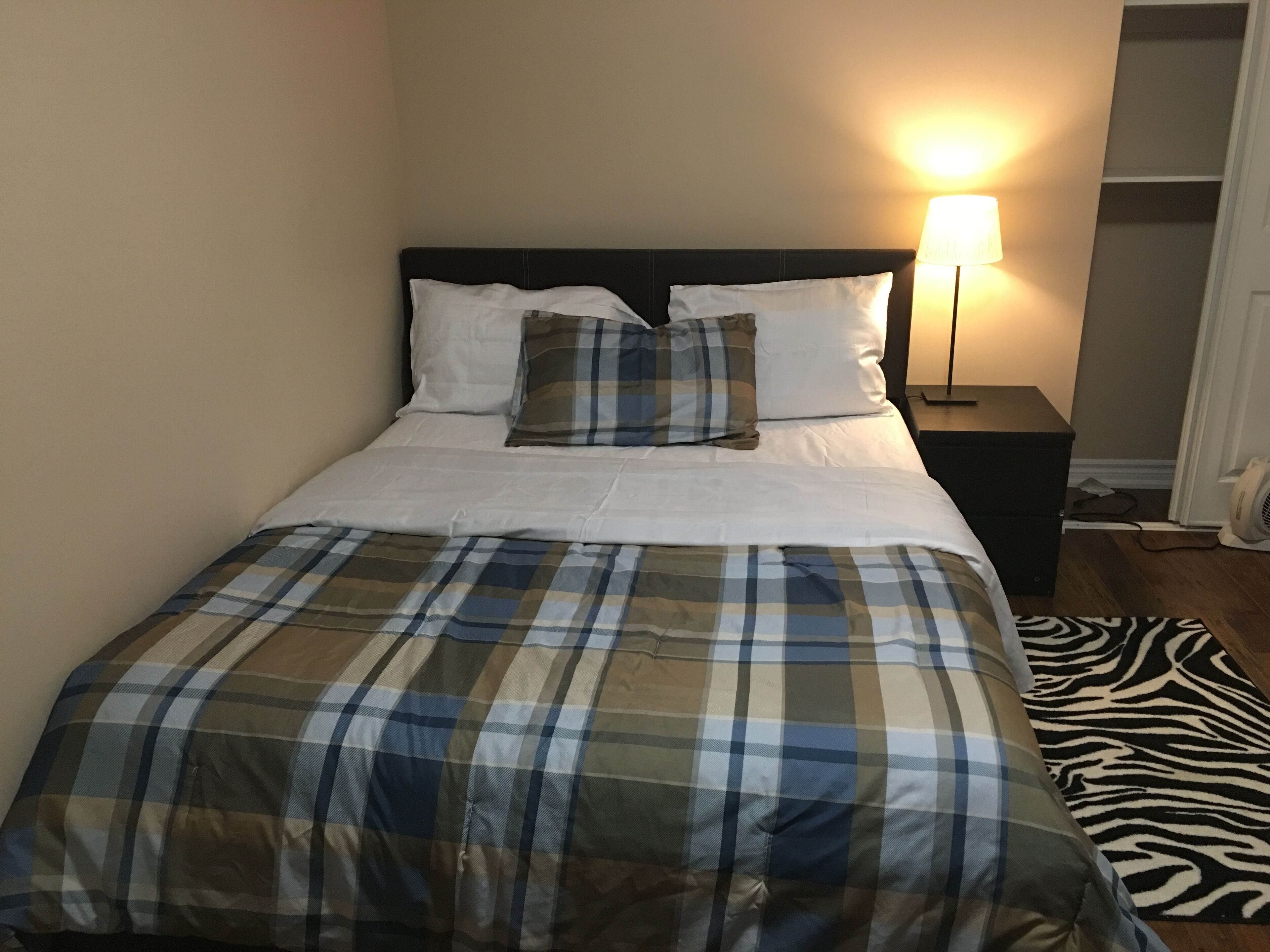 Una cama con colcha y almohadas a cuadros, una lámpara de noche y una alfombra con estampado de cebra.