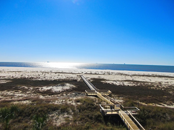A beach with a wooden boardwalk leading to the water, surrounded by sand and sparse vegetation.