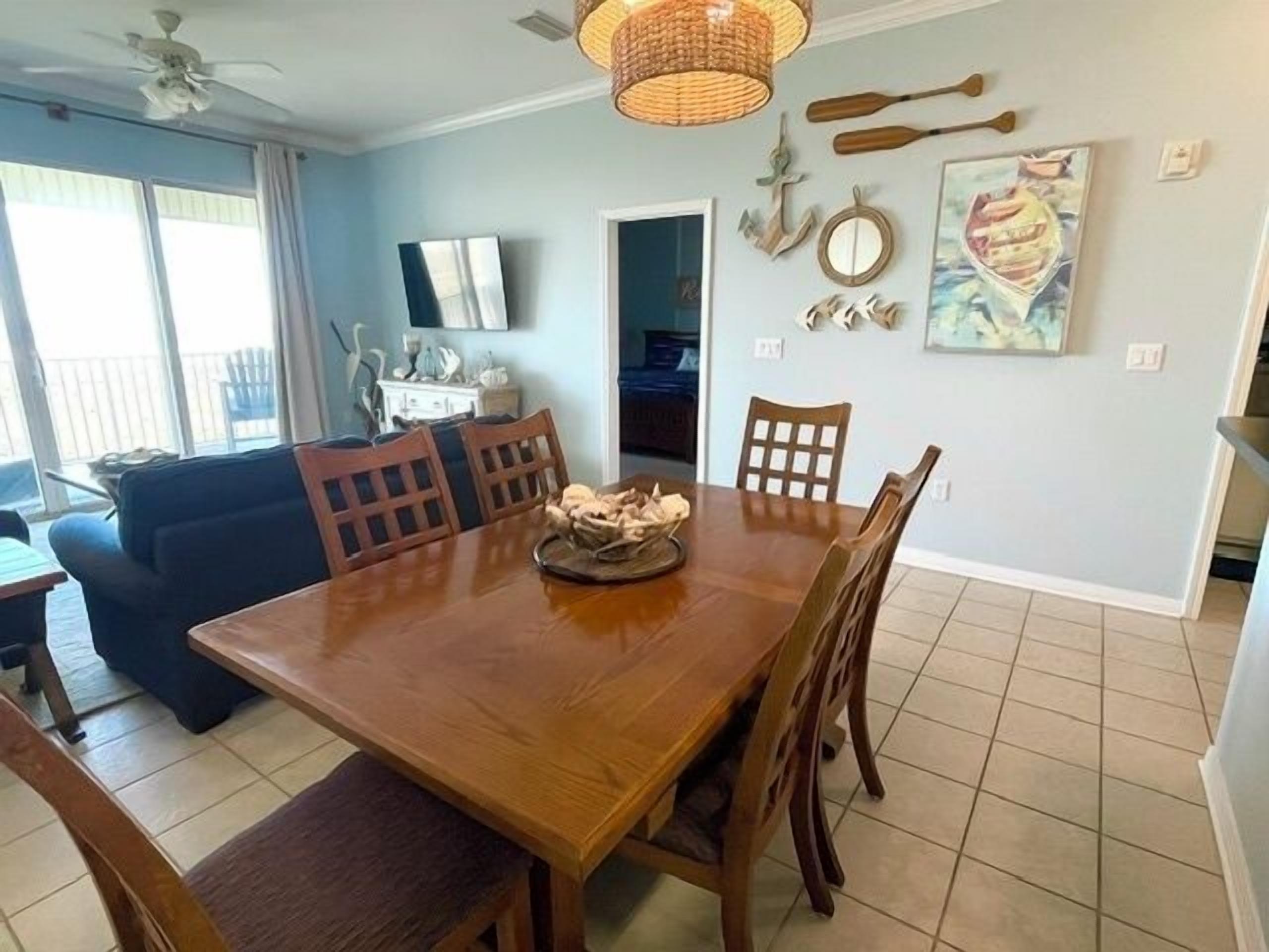 Un coin repas avec une table et des chaises en bois, un ventilateur de plafond et des décorations maritimes au mur.