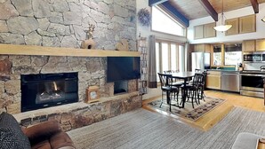 A spacious living area with a stone fireplace, a dining table with chairs, and a kitchen in the background. - 🌲Timberline B3E Standard 2-Bedroom + Loft ~ 2/bath ~Hot Tub~Pool~WiFi~Ski-in/out🌲 (Snowmass Village)