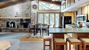 A spacious living area with a stone fireplace, a large TV, and a dining area with wooden furniture. - 🌲Timberline B3E Standard 2-Bedroom + Loft ~ 2/bath ~Hot Tub~Pool~WiFi~Ski-in/out🌲 (Snowmass Village)