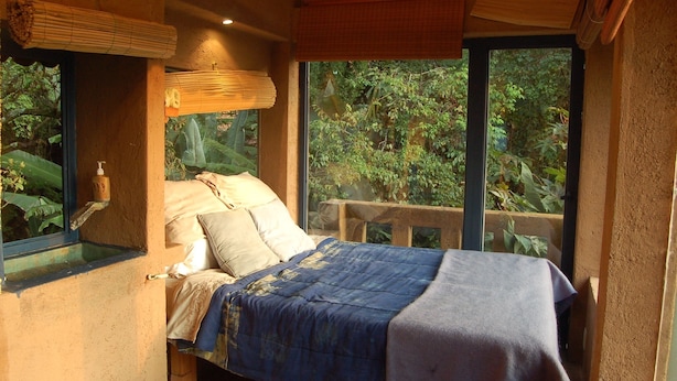 A bedroom with a bed, pillows, a window, and a view of greenery outside.