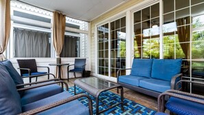 Un patio techado con mobiliario de mimbre, una mesa de vidrio y un sofá azul.