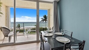 Een eetgedeelte met een tafel gedekt voor twee, uitzicht op de oceaan en een balkon met een witte stoel.