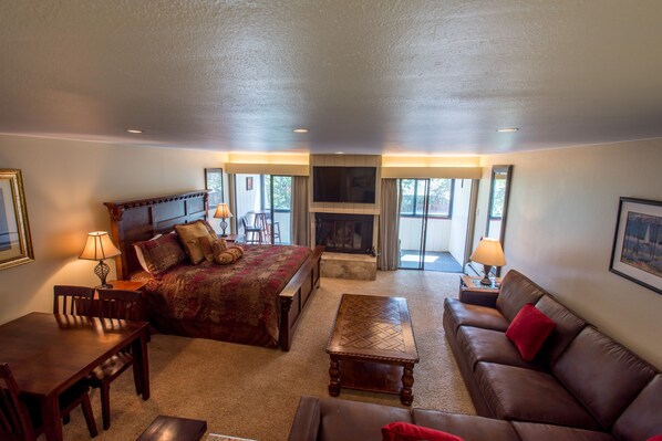 A spacious room with a large bed, a sofa, a dining table, and a fireplace.