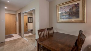 Un coin repas avec une table et des chaises en bois, un tableau encadré au mur et une porte donnant sur une autre pièce.