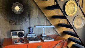 Een houten trap met decoratieve platen, een rode bureau met een radio, boeken en een transparante stoel.