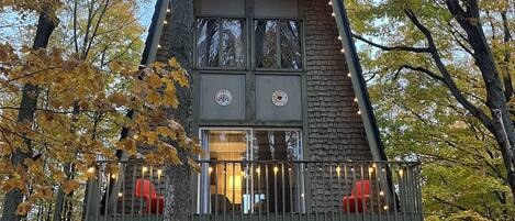 Una cabaña rústica con un balcón, una puerta de madera y un pequeño porche con plantas en macetas.