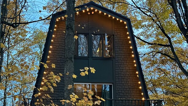 Een rustieke chalet met een bakstenen gevel, een rode garagedeur en lichtslingers.