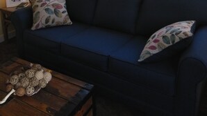Una sala de estar con un sofá azul, dos almohadas, una lámpara y una mesa de centro de madera.