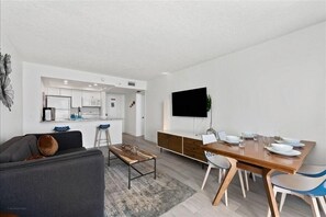 Ein modernes Wohnzimmer mit Sofa, Couchtisch und Essbereich, inklusive Fernseher und Esstisch.