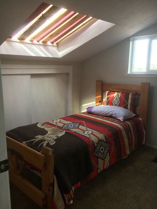 A bedroom with a skylight, a bed with a patterned bedspread, a wooden headboard, and a window.