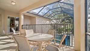 A sunlit patio with a round table and striped chairs, overlooking a swimming pool. - Homestead Cypress: Private Pool, Free Water Park, Near Disney (Kissimmee)