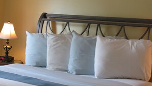 Una cama bien hecha con sábanas blancas, un cabecero, una lámpara de noche y un reloj digital que marca las 2:00.