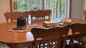Une table de salle à manger en bois, avec des chaises, un chapeau décoratif, un bol et un porte-serviettes.
