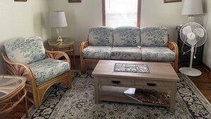 Un salon comprenant un canapé, deux fauteuils, une table basse, une lampe, un ventilateur et une fenêtre.