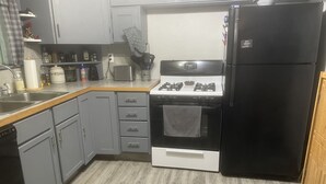 Une cuisine avec des meubles de couleur grise, un réfrigérateur noir, une cuisinière et un lave-vaisselle.