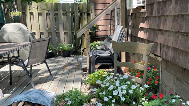 Une terrasse en bois avec des meubles d’extérieur, une chaise et des plantes en pot.