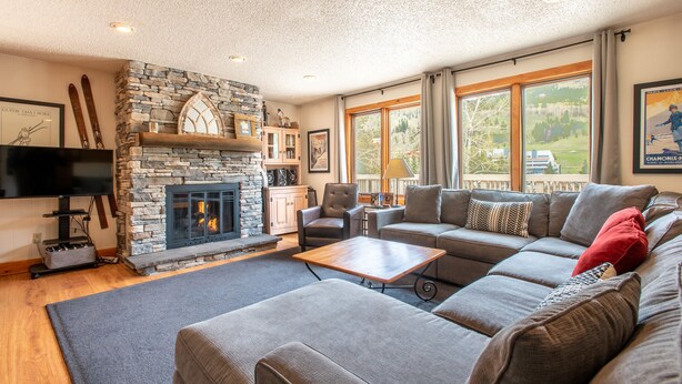 A cozy living room with a stone fireplace, a large sectional sofa, and a flat-screen TV. - Nice Ski-in/Walk-out condo, free wifi, & parking. (Copper Mountain)